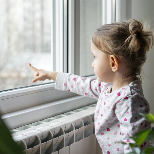 Little girl standing and looking through the window while her mother packing the moving boxes.