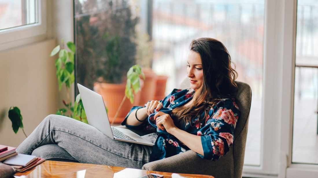 Vintage toned portrait of a young woman working at the table in the bright and beautiful apartment on the high floor in Belgrade, Serbia. She is wearing casual, everyday clothes and having a cup of coffee as well.